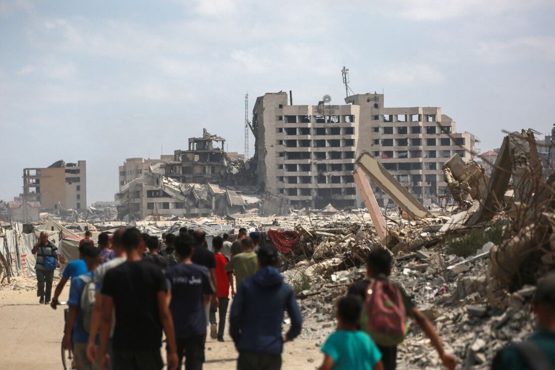 Palestinos caminham por uma estrada de terra em um campo de deslocados improvisado na orla da Cidade de Gaza