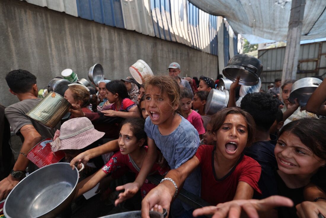 O horror da guerra: palestinos se reúnem para receber refeições preparadas em um centro de distribuição de alimentos no campo de refugiados de Nuseirat, no centro da Faixa de Gaza