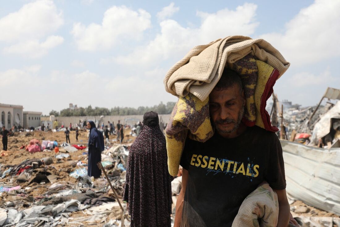 Um palestino deslocado carrega seus pertences após um ataque israelense a um campo de deslocados internos em Deir el-Balah, no centro da Faixa de Gaza.