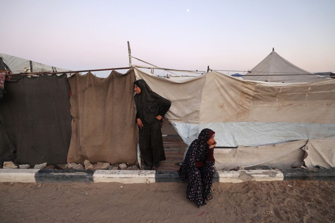 Mulheres palestinas deslocadas esperam do lado de fora das tendas de um acampamento em Bureij, no centro da Faixa de Gaza