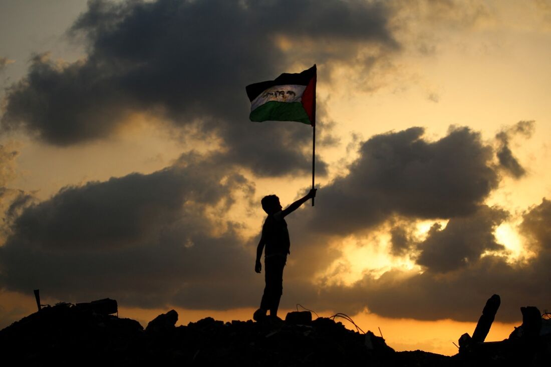 Uma criança palestina deslocada acena a bandeira nacional palestina enquanto está sobre os escombros de um prédio destruído no campo de refugiados de Bureij, no centro da Faixa de Gaza