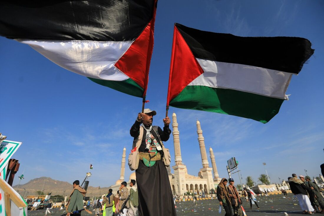 Um apoiador dos huthis do Iêmen agita bandeiras palestinas durante um comício condenando Israel e em apoio aos palestinos