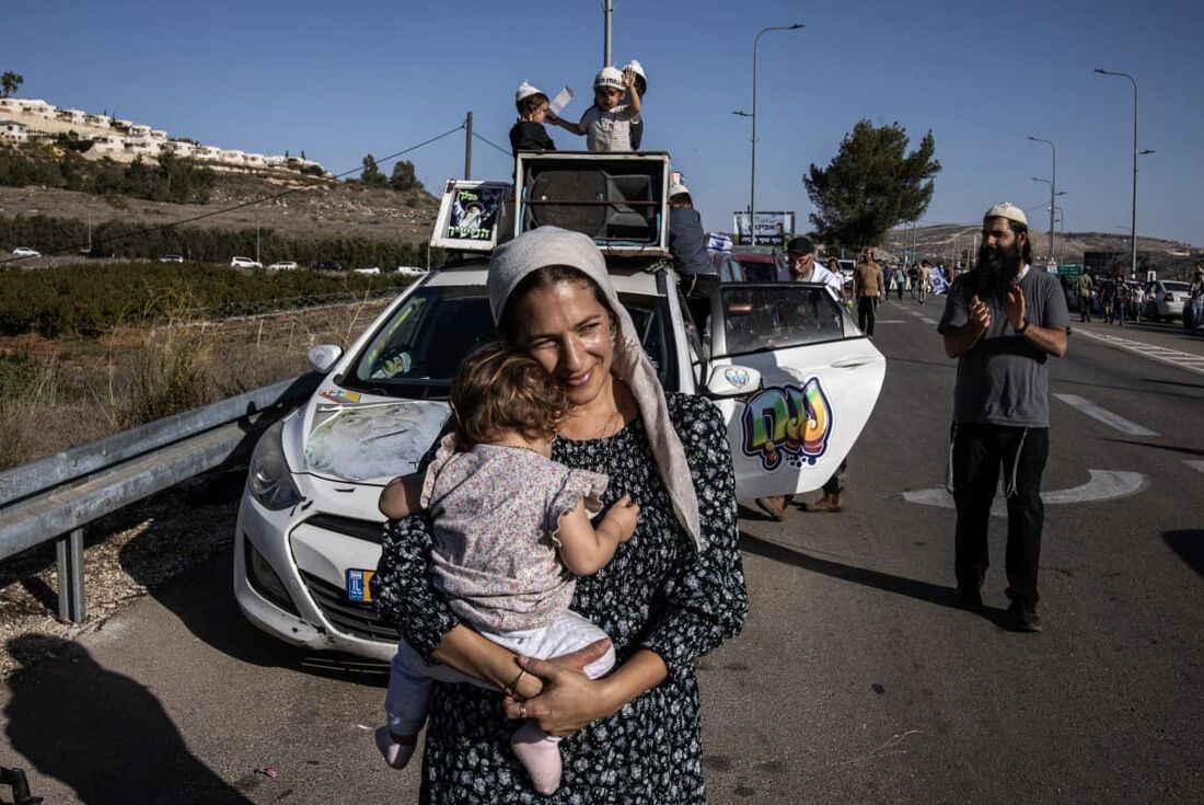 Uma colona israelense segura seu bebê enquanto espera com outros pelo retorno do refém libertado Avinatan Or no assentamento israelense de Shiloh, na Cisjordânia ocupada