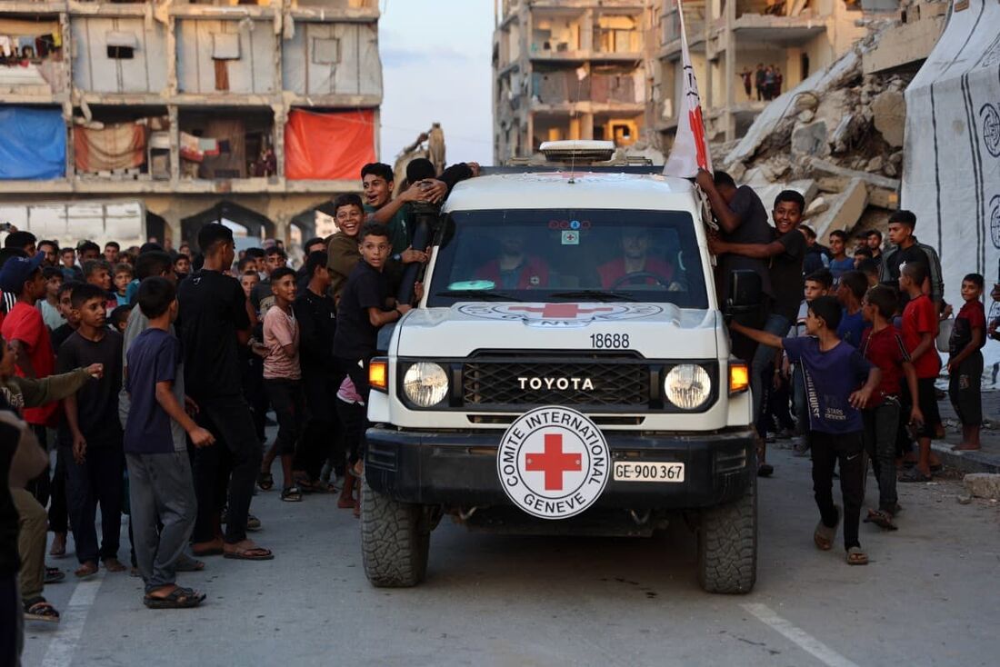 Crianças palestinas comemoram quando membros do Comitê Internacional da Cruz Vermelha (CICV) chegam a um local onde pessoas estão escavando com escavadeiras, supostamente em busca de corpos em Khan Yunis, no sul da Faixa de Gaza