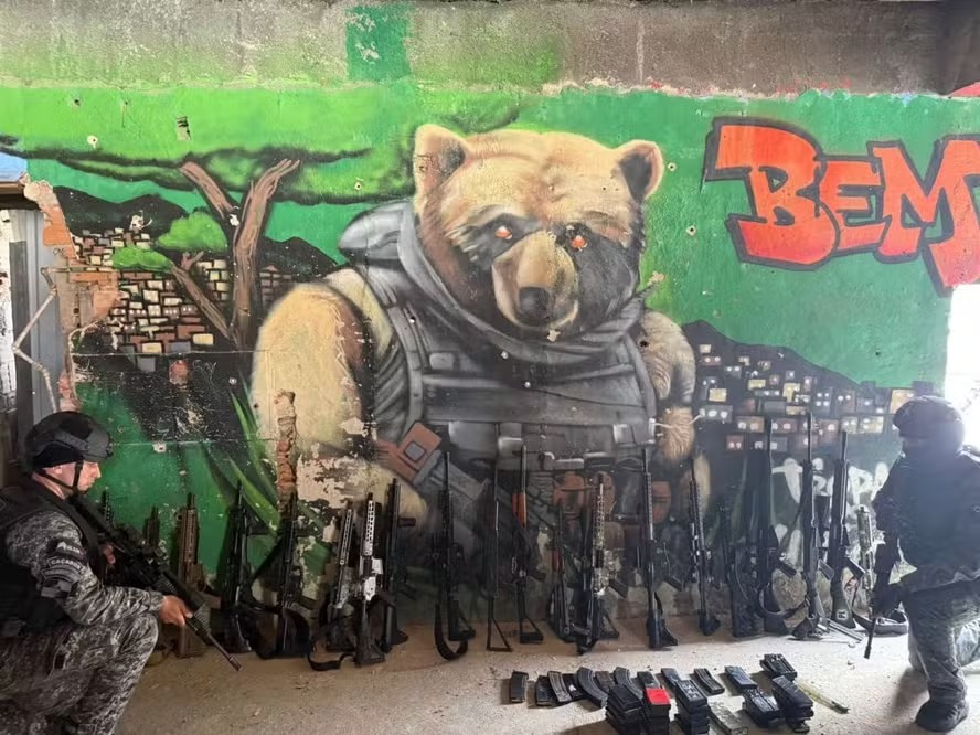 Fuzis apreendidos diante de muro com grafite em referência a Doca, conhecido também como Urso: armamento foi proibido em bailes na Penha