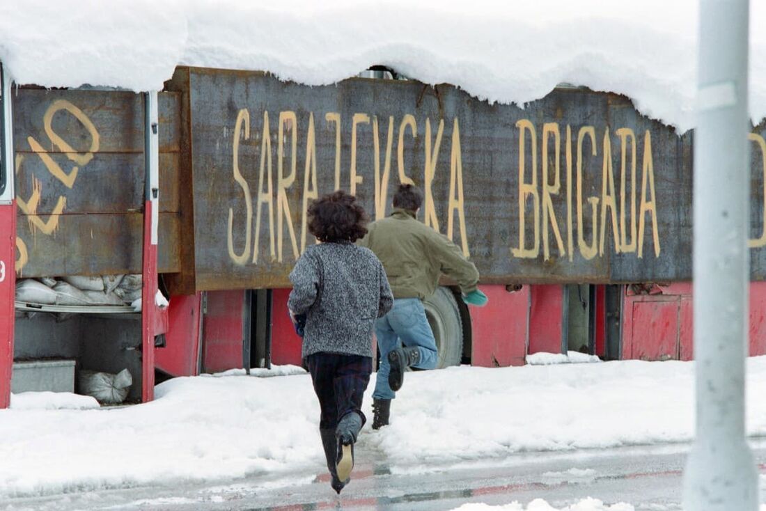 Um casal corre para se proteger de atiradores atrás de um ônibus com a inscrição "Brigada de Sarajevo", em 28 de março de 1993, em Sarajevo, durante a guerra da Bósnia.
