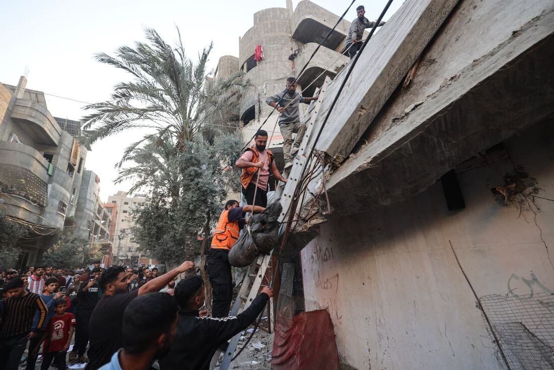 Membros da Defesa Civil palestina usam uma corda para retirar o corpo de uma vítima dos escombros de um prédio atingido por um ataque aéreo israelense no campo de refugiados de Nuseirat
