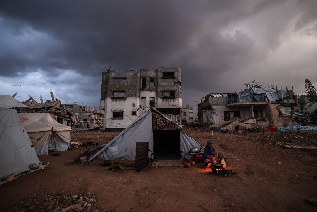 Uma mulher palestina deslocada senta-se junto a uma fogueira ao lado de sua tenda enquanto uma tempestade se aproxima no campo de Al-Bureij