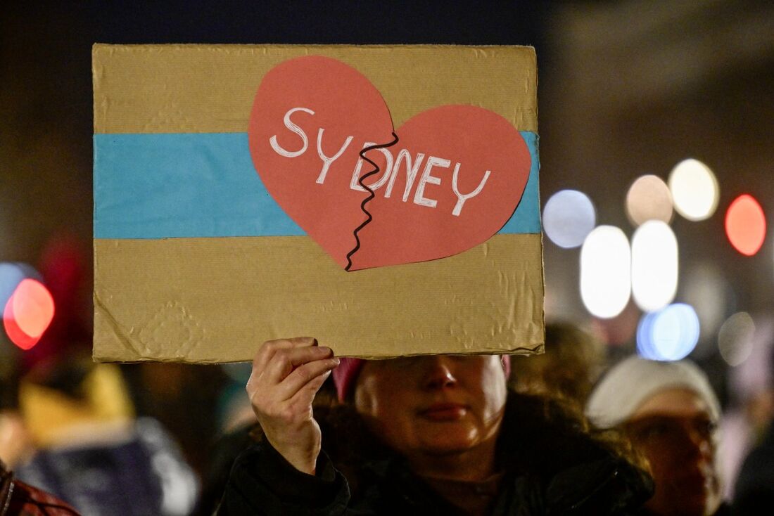 Uma mulher que participa da cerimônia de acendimento do grande candelabro menorá para celebrar o festival de Chanucá segura um cartaz com um coração e a inscrição "Sydney" em frente ao Portão de Brandemburgo