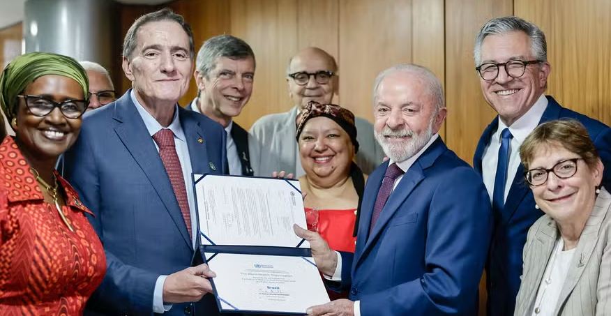 O diretor da Opas, Jarbas Barbosa, à esquerda, e o presidente do Brasil, Lula, à direita, seguram o certificado de eliminação da transmissão do HIV de mãe para filho como problema de saúde pública ao Brasil