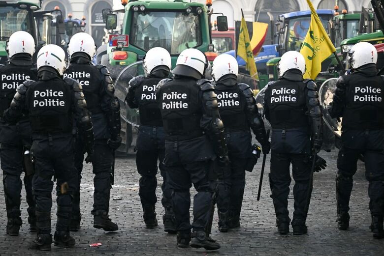 Policiais posicionam-se em frente a tratores perto do Parlamento Europeu durante um protesto de agricultores contra as reformas da Política Agrícola Comum (PAC) e acordos comerciais como o Mercosul, em Bruxelas. | Foto: AFP

