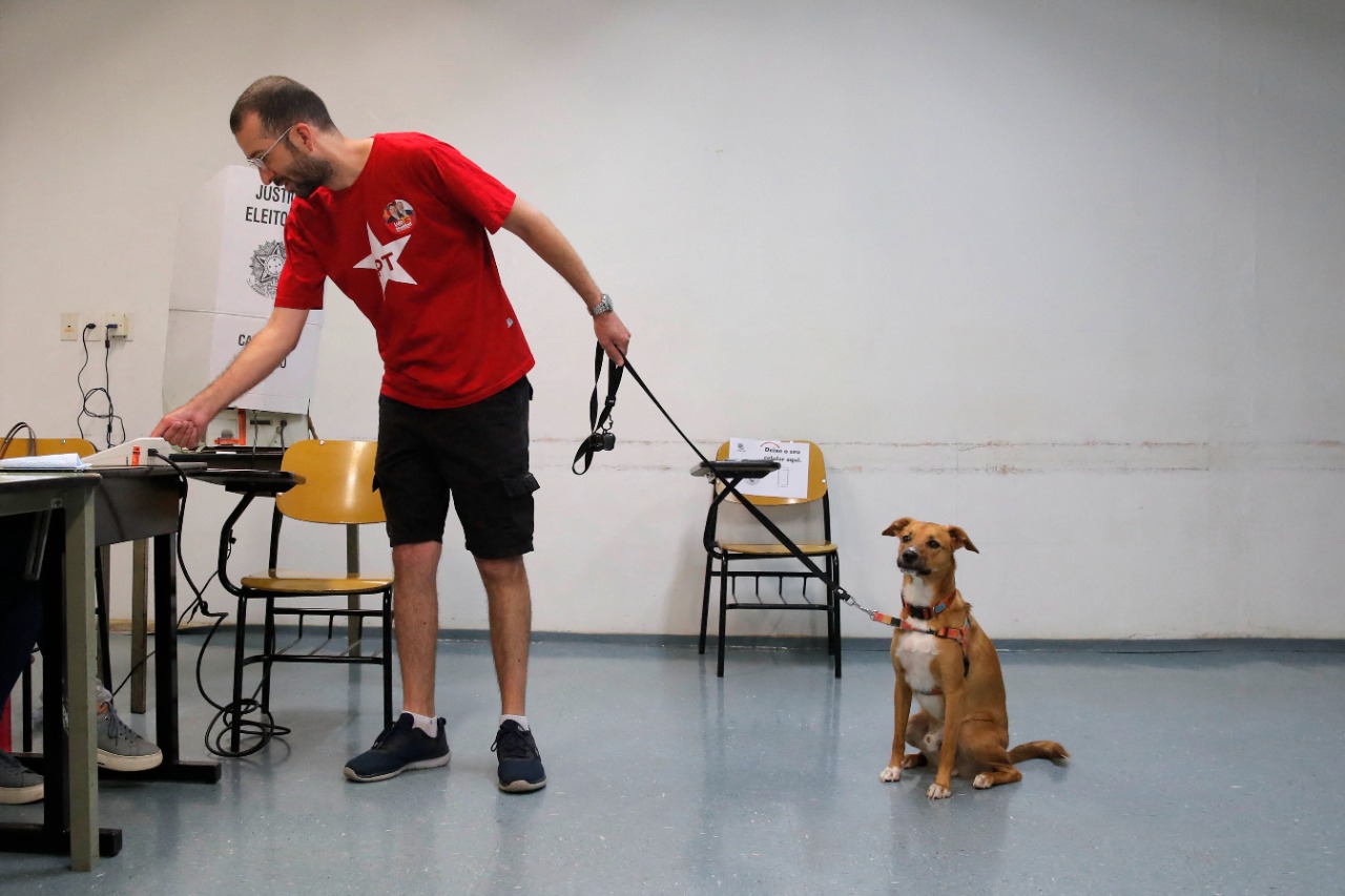 Um homem vota segurando a coleira de seu cachorro em uma estação de votação em São Paulo