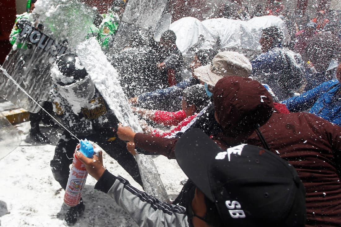 Pessoas marchando em homenagem aos que morreram durante confrontos com a polícia nas manifestações contra a presidente peruana Dina Boluarte, param a manifestação e brincam com a polícia borrifando água e espuma como tradição do carnaval em Puno, Peru