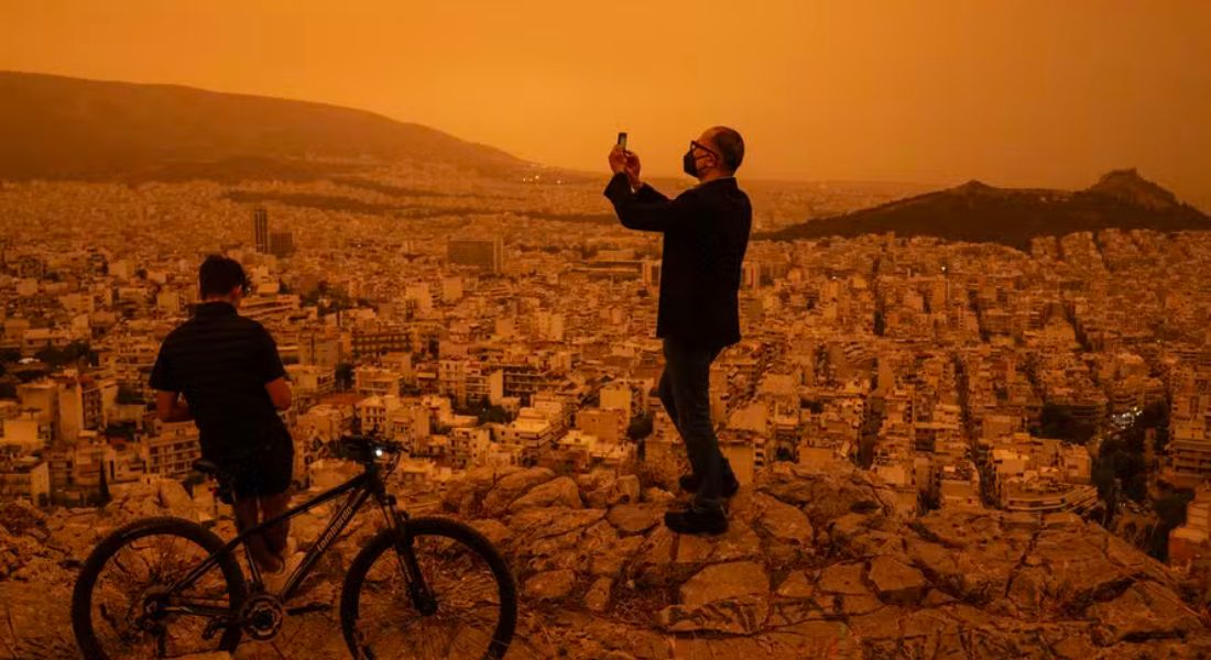 Um homem tira uma foto de Atenas a partir da colina Tourkovounia, após ventos do sul levarem ondas de poeira do Saara para a cidade