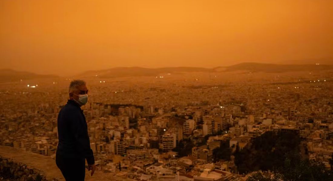 Um homem usando uma máscara facial olha para a cidade de Atenas da colina Tourkovounia, após ventos do sul carregarem ondas de poeira do Saara para a cidade