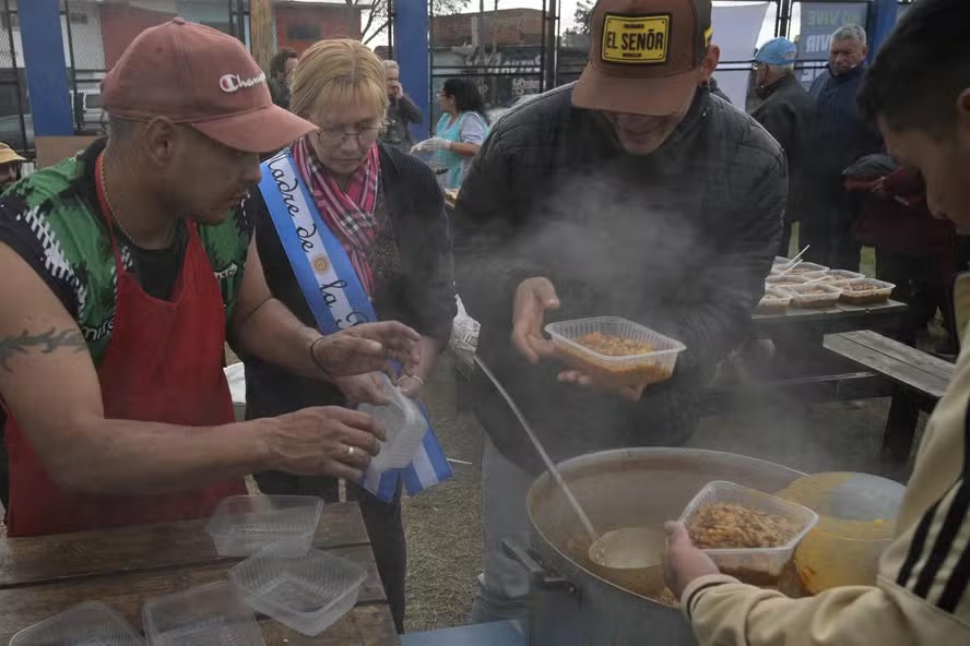 Um membro de uma cozinha comunitária serve sopa depois de uma missa presidida pelo bispo Oscar Ojea, no Santuário da Virgem de Caacupe, em Ciudad Evita, La Matanza, periferia de Buenos Aires