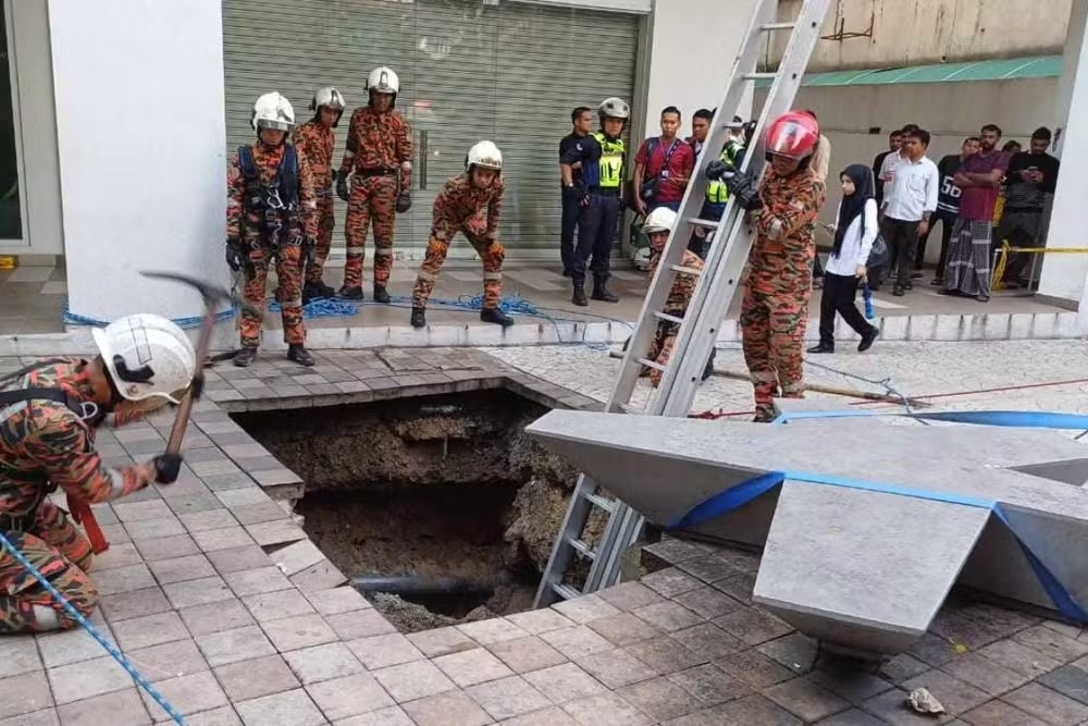 Equipes trabalham para resgatar uma mulher que caiu em um buraco em uma movimentada rua de Kuala Lumpur 