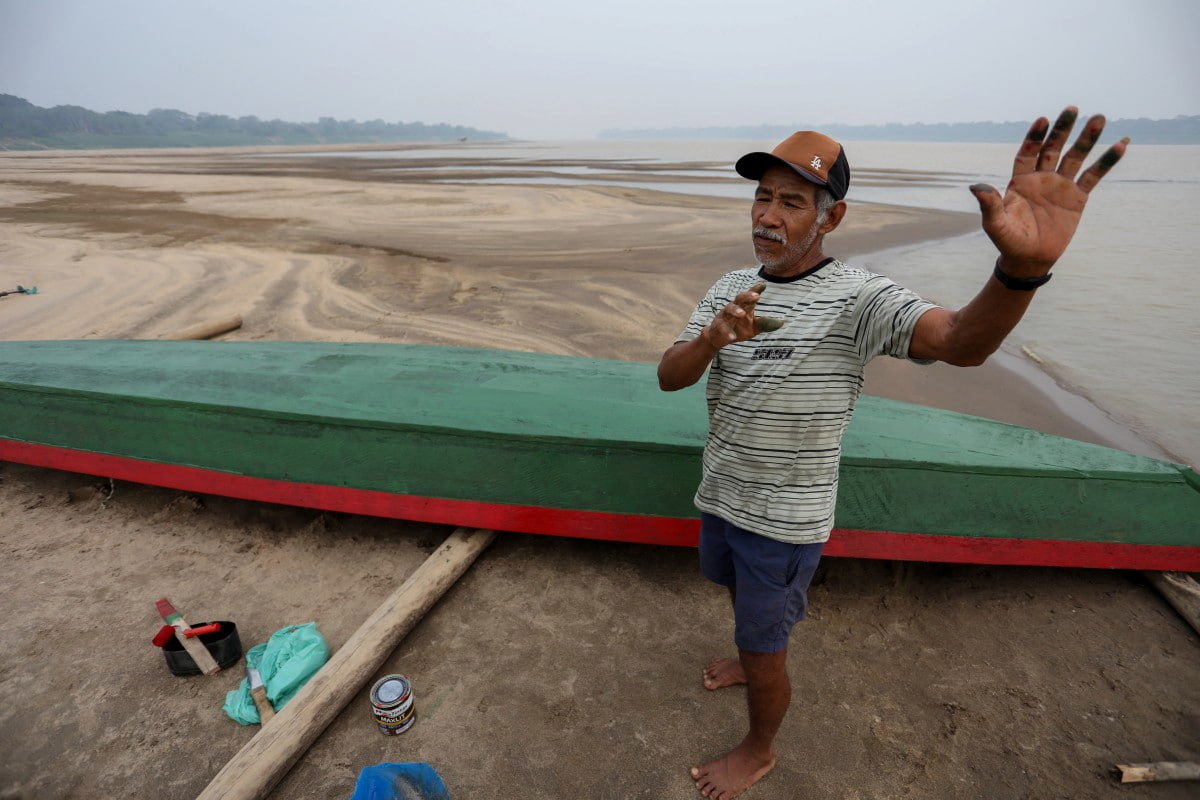 O fazendeiro Reis Santo Vieira, 69, conversa ao lado de uma canoa no leito seco do Rio Madeira, na Comunidade Paraizinho, em Humaitá, Amazonas