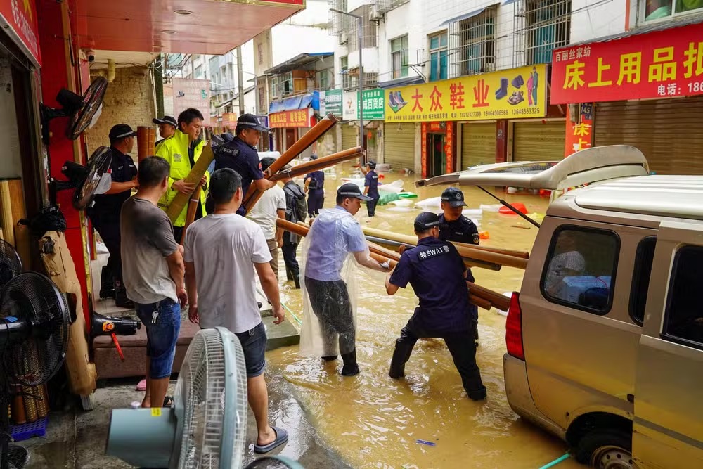 Socorristas ajudam comerciantes a remover equipamentos em uma rua inundada em Congjiang, na região de Guizhou 